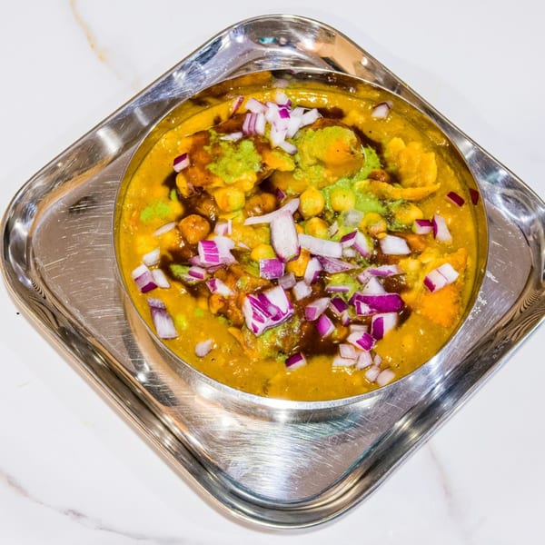A bowl of Indian chaat with chickpeas, sauces, and chopped red onions on a silver tray.