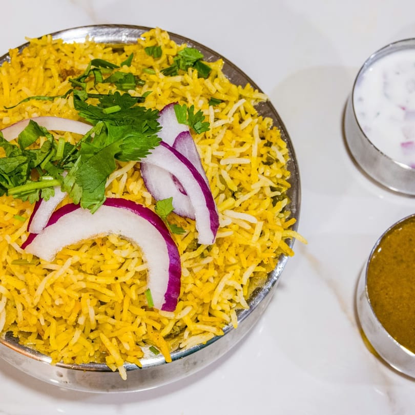 Yellow biryani rice with red onion and cilantro, served with two dipping sauces.