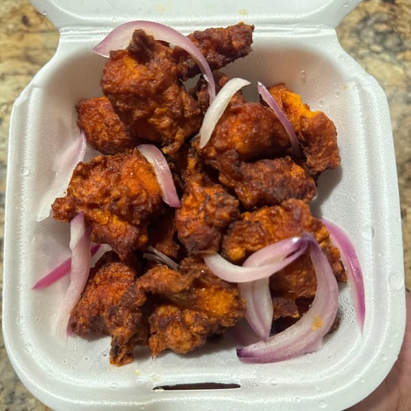 Crispy fried chicken pieces with red onion slices in a white takeout container.