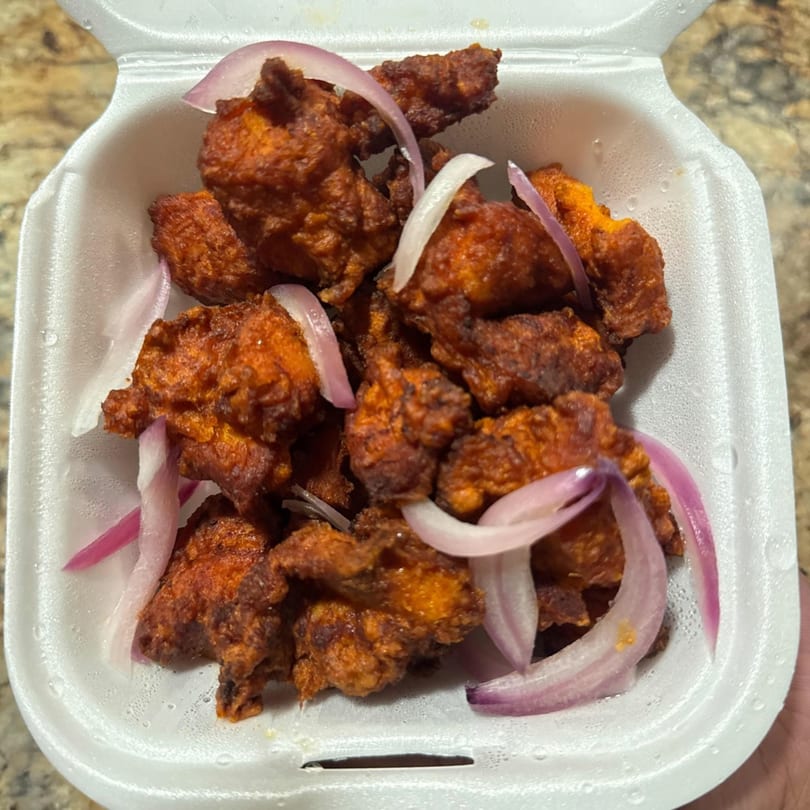 Crispy fried chicken pieces with red onion slices in a white takeout container.