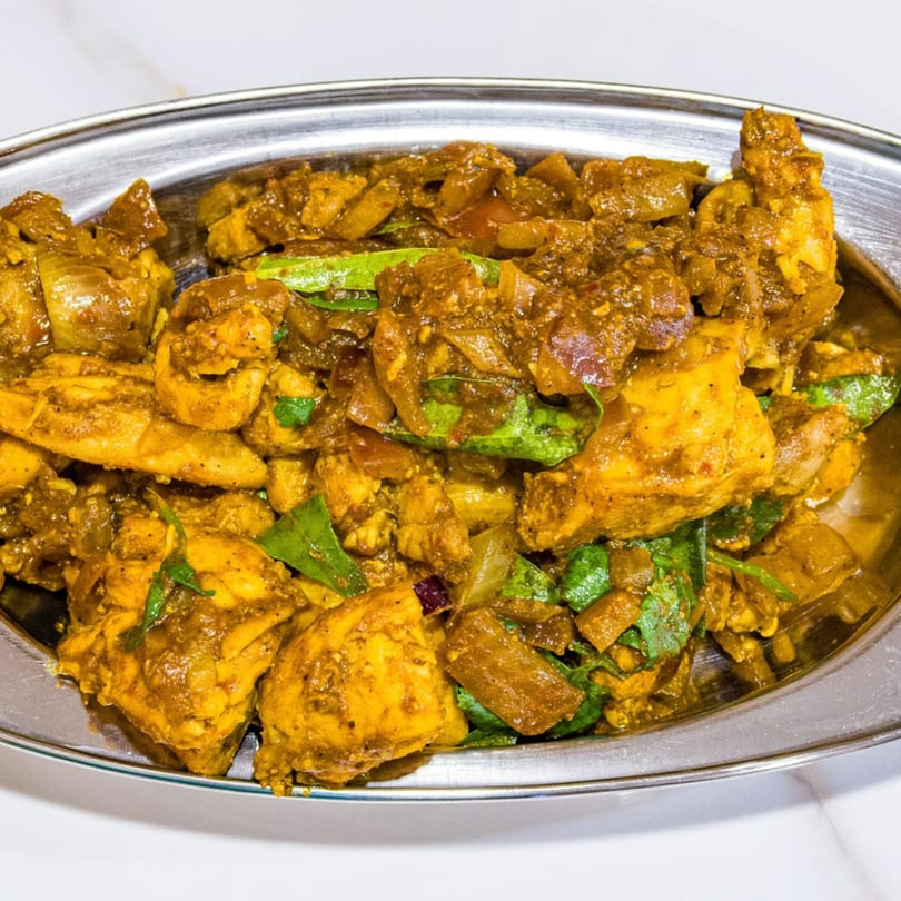 Close-up of a metal platter filled with golden chicken curry, onions, and green herbs.