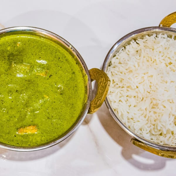 Two metal bowls, one with green curry and the other with white rice, on a white surface.