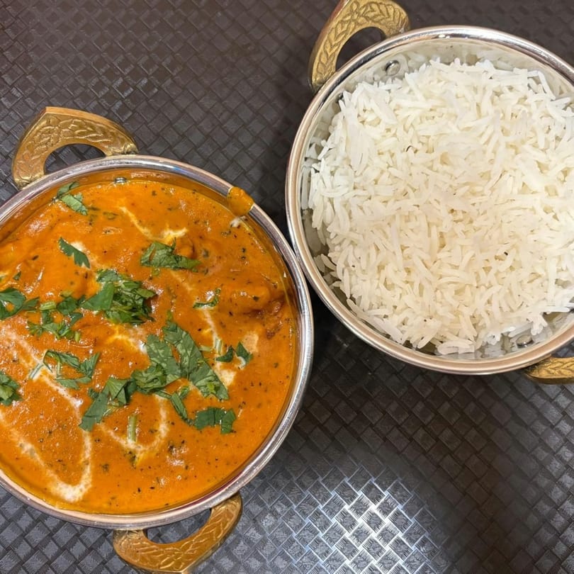 Two silver bowls, one with orange curry garnished with cilantro, the other with white rice.